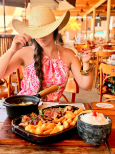 Mulher com chapéu de palha segurando drink e degustando prato típico em restaurante, produção audiovisual gastronômica